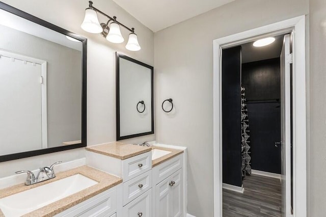 bathroom featuring double vanity, baseboards, a sink, and wood finished floors