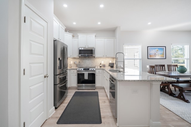 kitchen with sink, a center island with sink, white cabinetry, stainless steel appliances, and light hardwood / wood-style floors