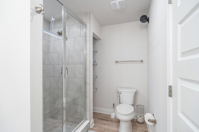 bathroom featuring a textured ceiling, a shower with door, hardwood / wood-style flooring, and toilet