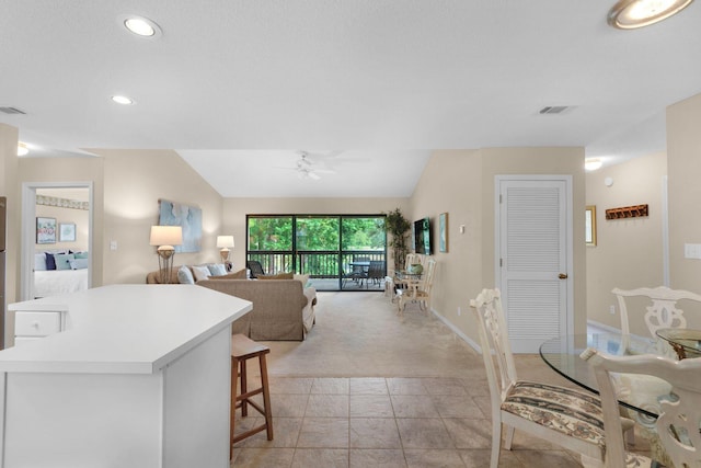 interior space with light carpet, lofted ceiling, a kitchen breakfast bar, and ceiling fan