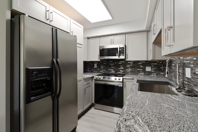 kitchen with appliances with stainless steel finishes, light stone countertops, sink, and backsplash