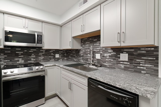 kitchen featuring appliances with stainless steel finishes, white cabinetry, sink, decorative backsplash, and light stone countertops