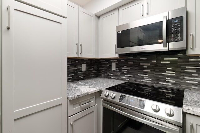 kitchen with light stone counters, backsplash, stainless steel appliances, and white cabinets