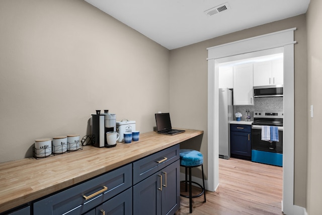 kitchen featuring blue cabinets, light hardwood / wood-style flooring, decorative backsplash, appliances with stainless steel finishes, and butcher block countertops