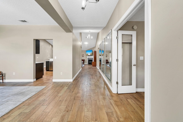 hall featuring a textured ceiling, an inviting chandelier, and light hardwood / wood-style flooring