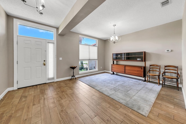 foyer entrance with a textured ceiling, light hardwood / wood-style flooring, and a notable chandelier