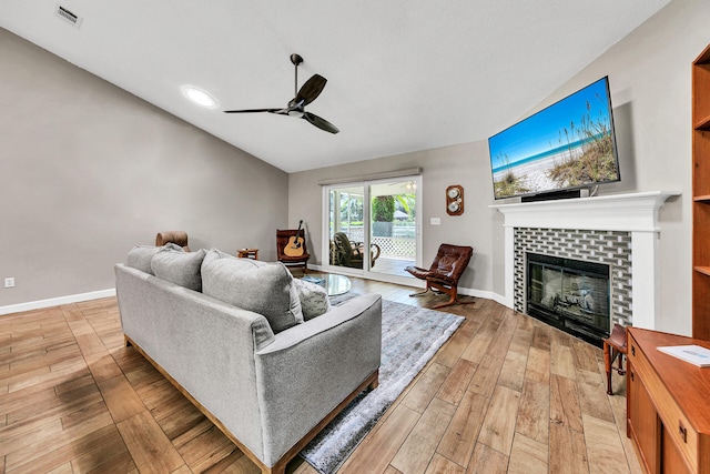 living room with ceiling fan, vaulted ceiling, a fireplace, and light hardwood / wood-style floors