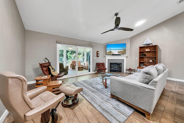 living room with wood-type flooring, vaulted ceiling, a tiled fireplace, and ceiling fan