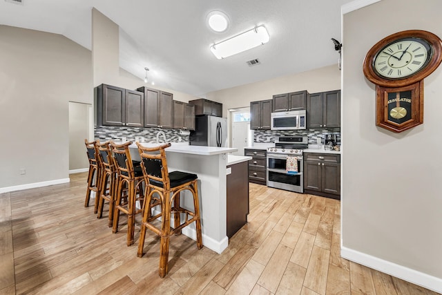 kitchen with lofted ceiling, a kitchen island, backsplash, appliances with stainless steel finishes, and a breakfast bar