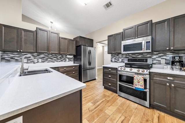 kitchen with light wood-type flooring, sink, lofted ceiling, decorative backsplash, and stainless steel appliances