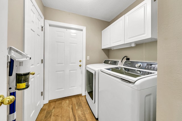 laundry area featuring a textured ceiling, light hardwood / wood-style floors, washer and dryer, and cabinets