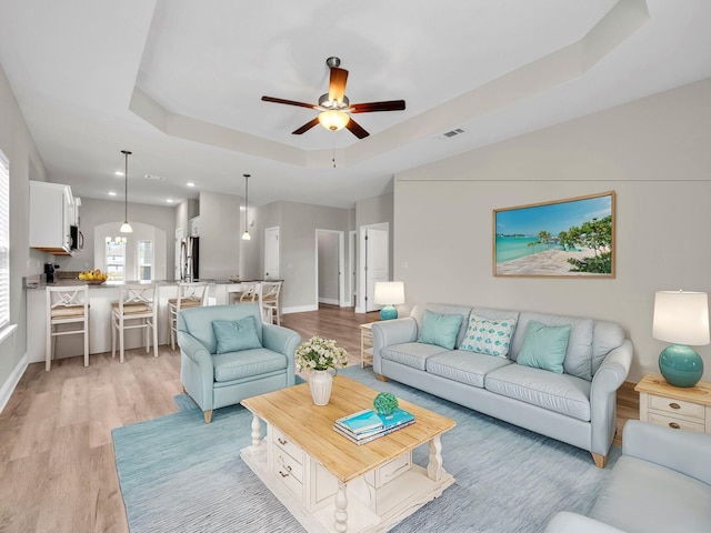 living room featuring light wood-type flooring, a tray ceiling, and ceiling fan