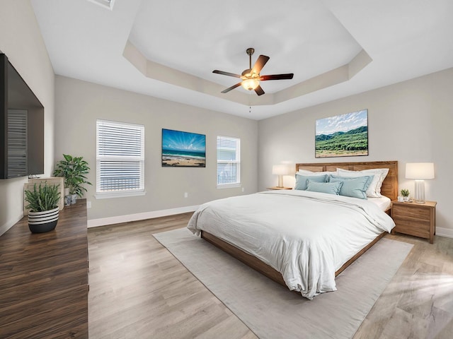 bedroom featuring ceiling fan, light wood-type flooring, and a tray ceiling