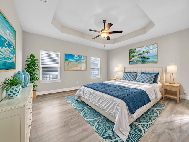 bedroom with light hardwood / wood-style flooring, ceiling fan, and a raised ceiling