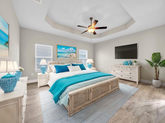 bedroom with light hardwood / wood-style flooring, a tray ceiling, and ceiling fan