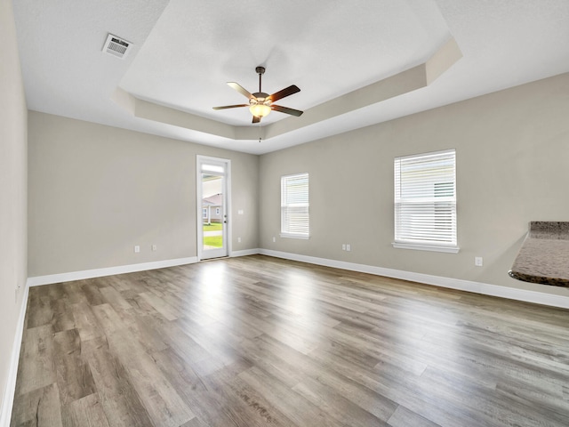 unfurnished living room featuring light wood-type flooring, a tray ceiling, and ceiling fan