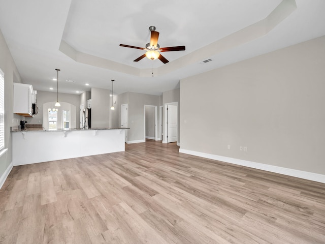 unfurnished living room featuring ceiling fan, light wood-type flooring, and a tray ceiling