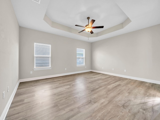 spare room featuring light hardwood / wood-style floors, ceiling fan, and a raised ceiling