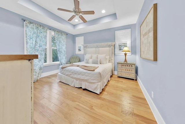 bedroom featuring ceiling fan, a tray ceiling, and light hardwood / wood-style flooring