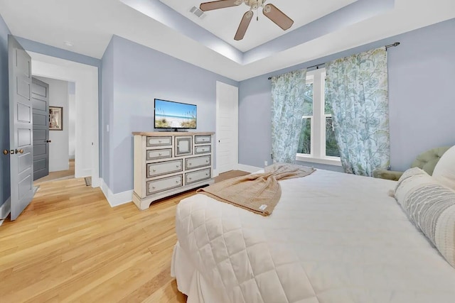 bedroom with ceiling fan, light hardwood / wood-style floors, and a tray ceiling