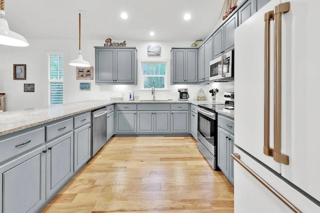 kitchen with gray cabinets, appliances with stainless steel finishes, hanging light fixtures, light wood-type flooring, and sink