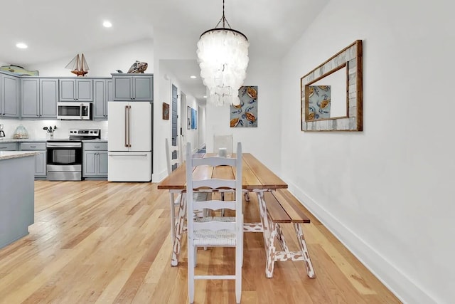 dining space with an inviting chandelier, vaulted ceiling, and light hardwood / wood-style flooring