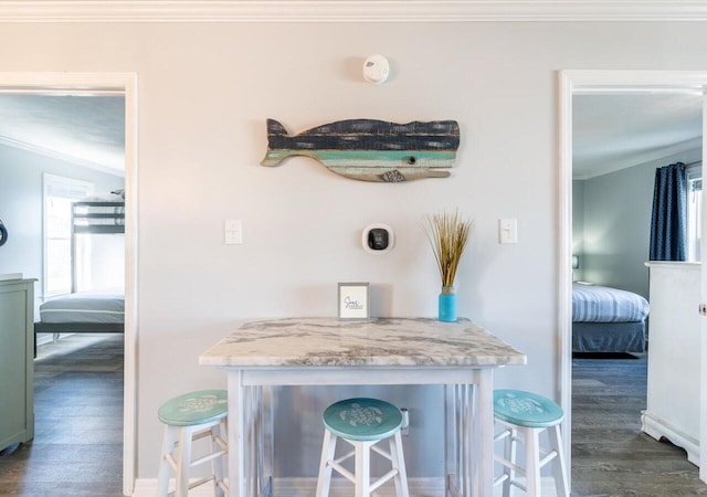 kitchen with crown molding, dark wood-type flooring, light stone counters, and a breakfast bar