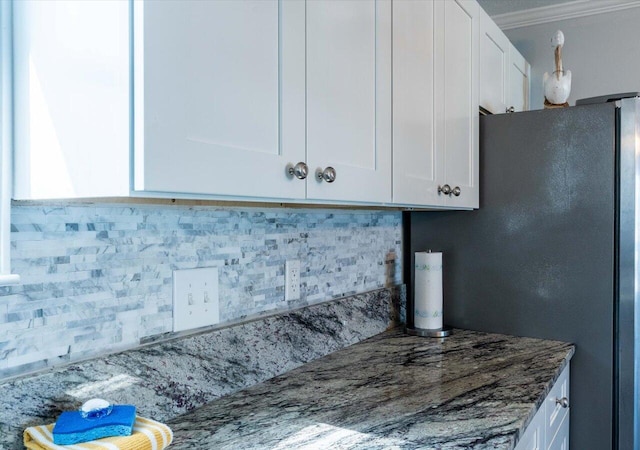 kitchen with decorative backsplash, stainless steel fridge, white cabinets, crown molding, and dark stone counters