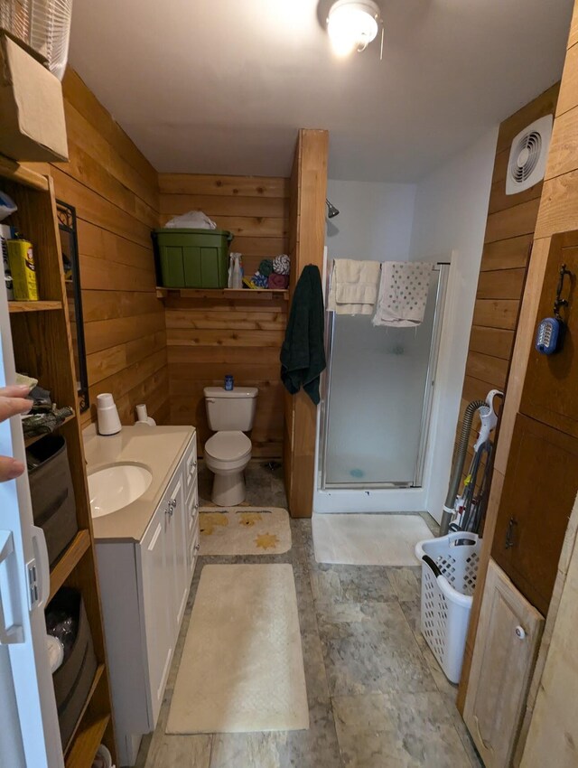 bathroom with wood walls, an enclosed shower, vanity, and toilet