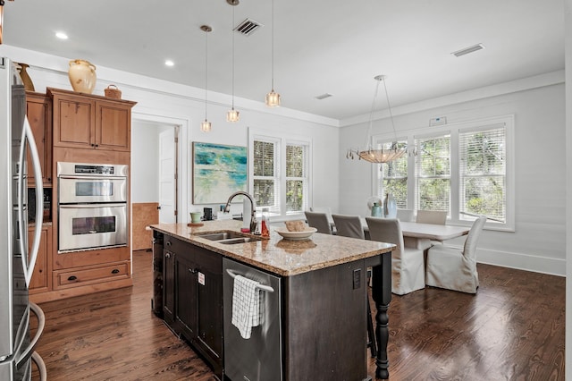 kitchen with light stone countertops, appliances with stainless steel finishes, sink, a center island with sink, and decorative light fixtures