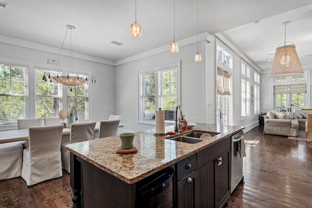 kitchen featuring a kitchen island with sink, sink, light stone countertops, decorative light fixtures, and dark brown cabinetry