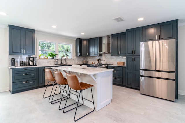 kitchen featuring light stone counters, wall chimney exhaust hood, backsplash, appliances with stainless steel finishes, and a center island