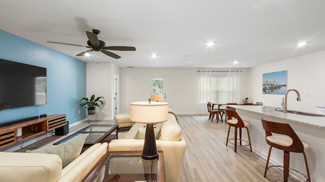 living room featuring ceiling fan, light wood-type flooring, and sink