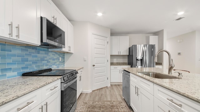 kitchen with light stone counters, stainless steel appliances, white cabinets, sink, and light hardwood / wood-style flooring