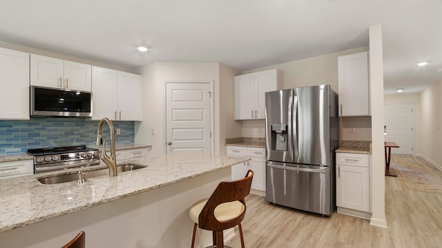 kitchen with light wood-type flooring, white cabinetry, appliances with stainless steel finishes, a breakfast bar, and light stone countertops