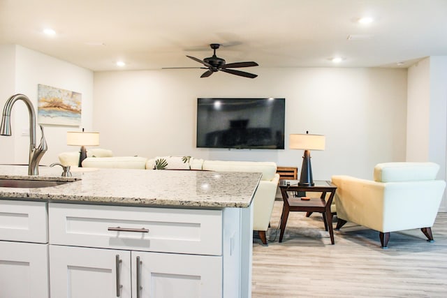 kitchen with white cabinets, light stone countertops, open floor plan, and a sink