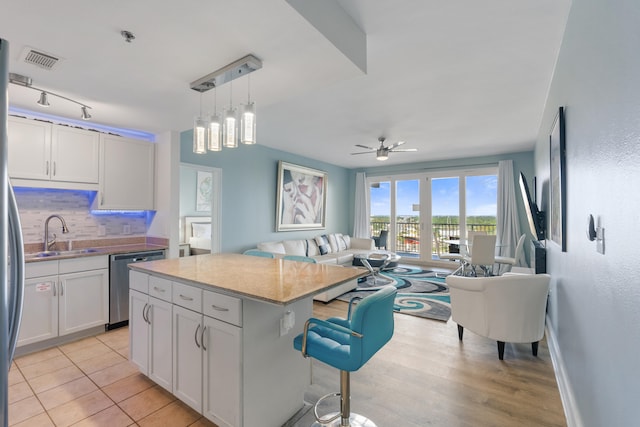 kitchen featuring ceiling fan, a kitchen island, stainless steel dishwasher, decorative light fixtures, and white cabinetry