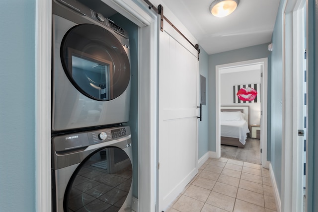 clothes washing area with a barn door, stacked washer and dryer, and light tile patterned floors