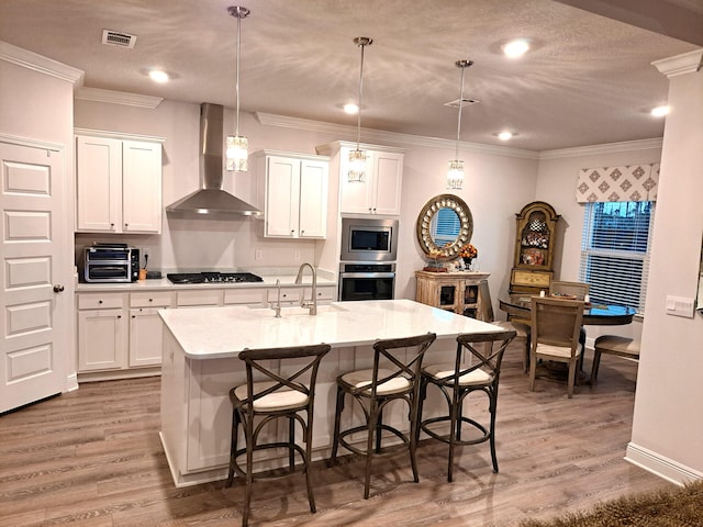 kitchen featuring stainless steel appliances, white cabinetry, hanging light fixtures, and wall chimney range hood