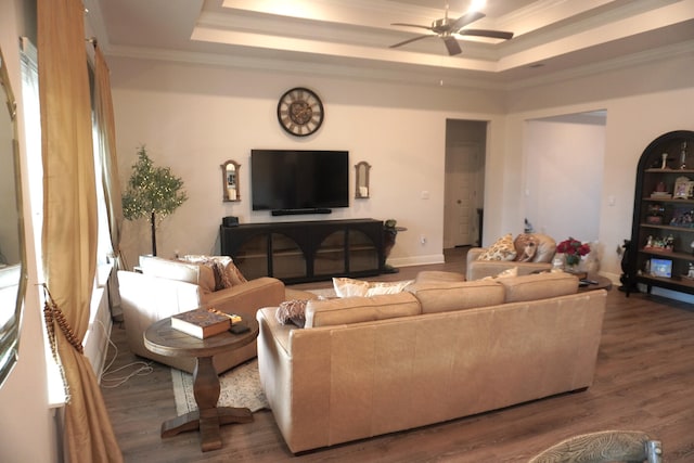 living room with ceiling fan, a tray ceiling, ornamental molding, and wood-type flooring