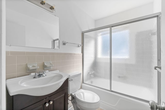 full bathroom with tile walls, vanity, bath / shower combo with glass door, and toilet