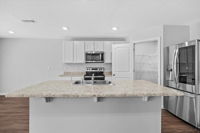 kitchen with dark hardwood / wood-style flooring, stainless steel appliances, sink, white cabinets, and an island with sink