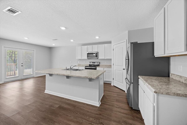 kitchen featuring a center island with sink, dark hardwood / wood-style flooring, white cabinetry, and appliances with stainless steel finishes