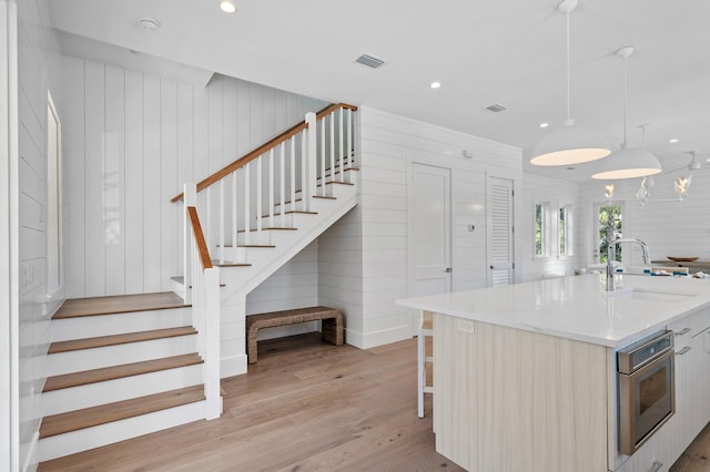 kitchen with pendant lighting, light hardwood / wood-style floors, sink, wood walls, and a center island with sink