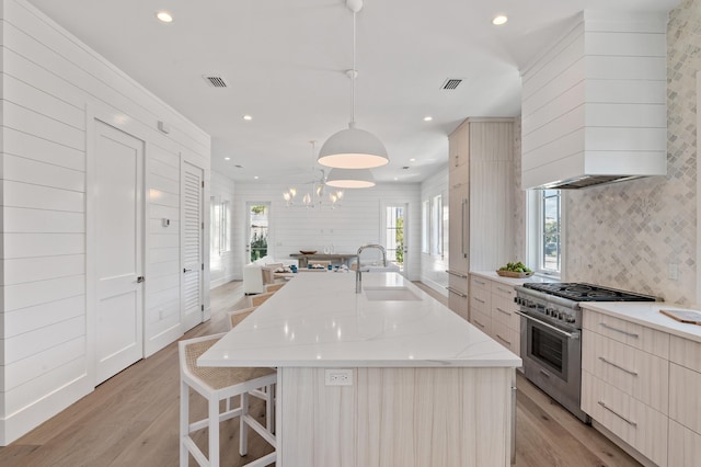 kitchen featuring high end stainless steel range oven, decorative light fixtures, a spacious island, and sink