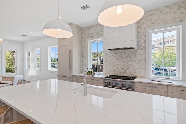 kitchen with light stone countertops, pendant lighting, sink, and stainless steel stove