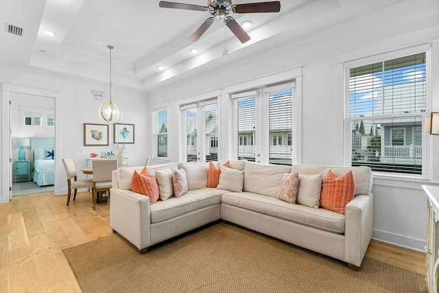 living room featuring ceiling fan, light hardwood / wood-style flooring, and a tray ceiling