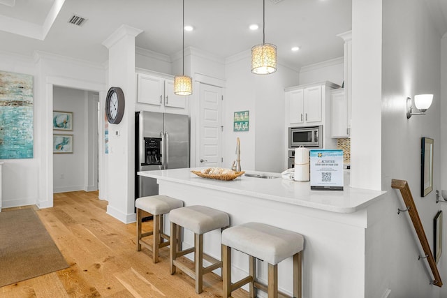 kitchen with appliances with stainless steel finishes, hanging light fixtures, white cabinets, kitchen peninsula, and light wood-type flooring