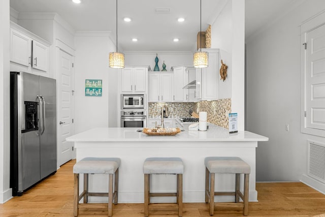 kitchen featuring appliances with stainless steel finishes, hanging light fixtures, kitchen peninsula, and light hardwood / wood-style flooring