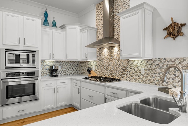 kitchen with sink, wall chimney exhaust hood, backsplash, white cabinetry, and stainless steel appliances